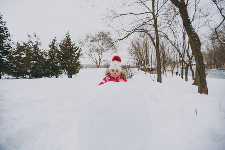 美丽的小女孩穿着冬天温暖的衣服和帽子，在雪地公园或户外森林里玩雪球堆雪人。 假日的冬季乐趣休闲。 家庭生活方式观念