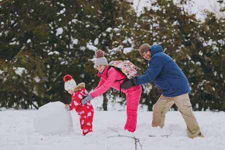 家庭妇女男人小女孩穿着温暖的衣服，在雪地公园或户外森林里堆雪人互相推搡。 假日的冬季乐趣休闲。 家庭生活方式观念