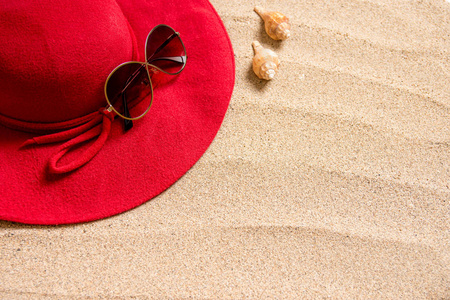 红色帽子在沙滩上，带太阳镜贝壳和复制空间的文本。