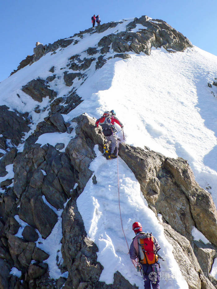 登山者在陡峭的雪和岩石表面上,在通往阿尔卑斯山的高山峰的路上.