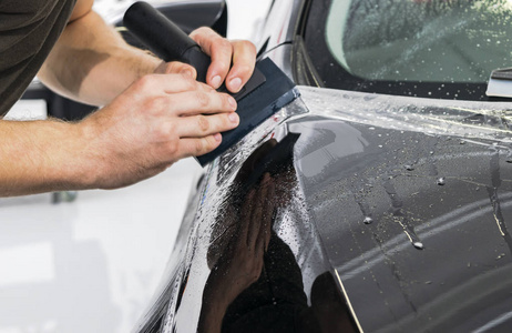 汽车包装专家把乙烯基箔或薄膜放在汽车上。 汽车上的保护膜。 用工具在汽车上涂上保护膜。 汽车细节。 透明薄膜。 汽车油漆保护。 