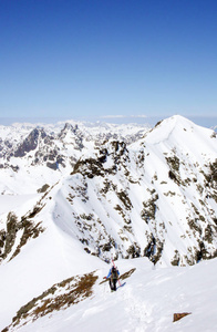 一名男性越野滑雪者在瑞士阿尔卑斯山攀登和徒步旅行一条长而暴露的狭窄雪岭，途中到达Silvretta山脉的一座高山峰。