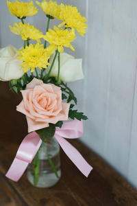 白色墙壁背景的木桌上的花瓶上有可爱的小粉玫瑰