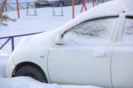 白色汽车的前部覆盖着一层雪。 把车停在白雪覆盖的停车场里。