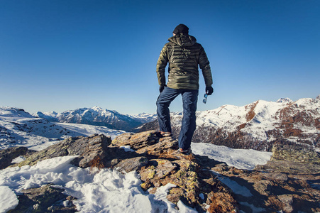 s back with sunglasses in hand, looks at the mountainous horizon