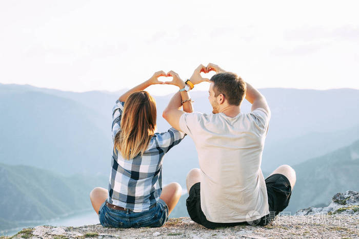 一对相爱的夫妇用交叉的双手做心坐在地上欣赏湖景