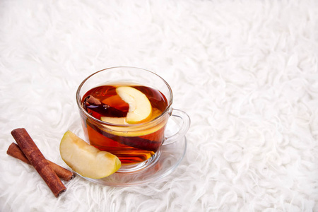 热饮苹果茶与肉桂棒八角茴香和丁香。 季节性苹果打孔杯在毛皮背景。