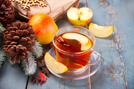 热饮苹果茶与肉桂棒八角茴香和丁香。 季节性苹果打孔杯在木制背景上。