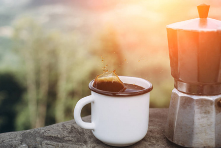 在日落时，在大自然的背景上喝杯热咖啡和咖啡机。 概念冒险活动户外度假。 夏令营