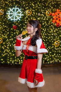 快乐微笑的圣诞老人女孩是可爱的红色西装和手拿香槟与圣诞树背景庆祝圣诞节和新年快乐。