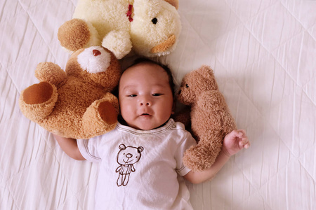 亚洲可爱的婴儿新生的微笑和快乐的好心情在床上与泰迪熊顶视图。