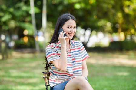 女人电话快乐美丽的年轻女孩微笑着在公园里谈论手机交流户外快乐的女人学生使用技术智能手机度假放松的女人打手机