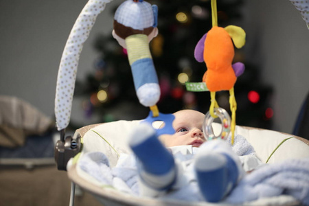 新生的滑稽婴儿躺在摇篮里，靠着圣诞树玩玩具
