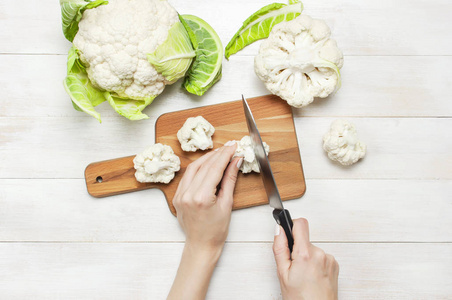 女手用刀切菜花在砧板上,厨房毛巾在乡村白色的木制背景上,俯视平面