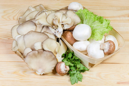 在浅色的木桌上，在木篮中种植不同的生香槟榔蘑菇和带绿色的牡蛎蘑菇