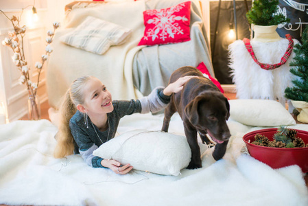 可爱的金发女孩在家里和一只狗马拉穆特和拉布拉多在家里的装饰房间里玩圣诞节
