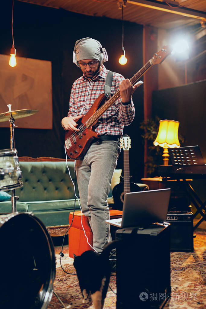 专注的高加索音乐家演奏低音吉他耳朵上有耳机完整的长度
