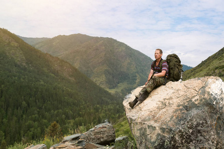 一个背着背包的人坐在一块大石头上,看着风景.照片