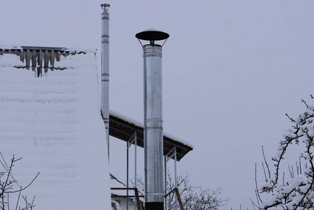 对阴暗的灰色天空长灰色的金属烟囱管在屋顶上的雪对天空照片
