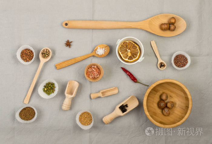木制勺子组成，各种香料和整个坚果在灰色织物背景，平躺，俯视