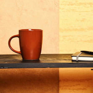 热饮料和休闲时间的概念。现代室内低黑桌上的茶或咖啡。笔记本上有书签, 钢笔和棕色杯子在桌子附近的墙上。带钢笔和新杯子的日记本在室