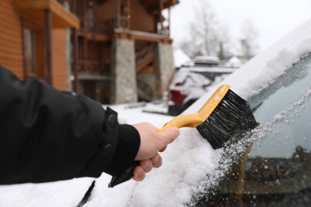 男人用刷子在户外特写镜头从雪地上清洁汽车挡风玻璃