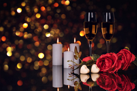 两杯香槟玫瑰蜡烛和两颗心形巧克力在黑色背景上，背景中有灯光。 爱情情人节概念