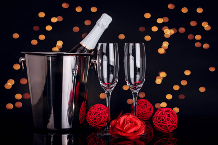 香槟瓶在桶里，两个酒杯和红玫瑰在黑色背景上，背景上有灯光。 爱情情人节概念