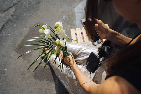 年轻的女人坐在城市街道上的长凳上，手里拿着一束白花。