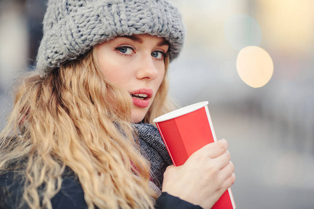 女人在街上散步时喝她的热咖啡。穿着冬装喝着热咖啡的时髦微笑女人的肖像。女性冬季风格。图像