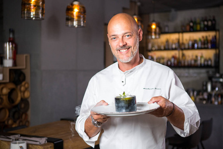 一个英俊的意大利男人秃顶,胡子是白色的制服厨师,在一家餐馆里,手里