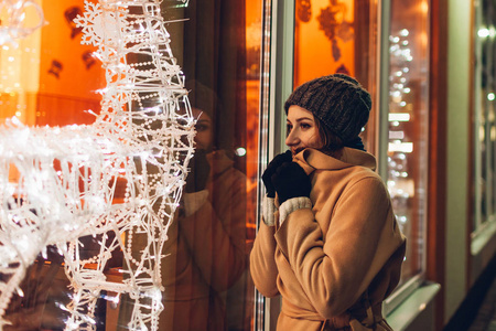 年轻的女人在城市里散步，晚上看装饰的圣诞手提箱。 新年概念