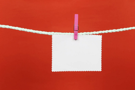 空注纸挂在晾衣绳上，并有红色背景的复制空间，以便在您的工作概念中进行设计。