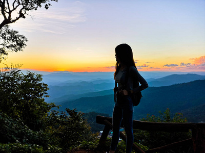 美丽的亚洲年轻女性旅行者徒步旅行与背包，一个山的自然背景。亚洲女性旅行者独自放松。站在泰国清迈看日落的人。