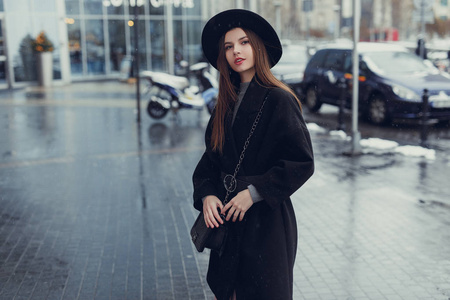 年轻的时尚女性走在城市街道上，戴着黑色帽子环顾四周，微笑着拍照。 复制空间。 图像
