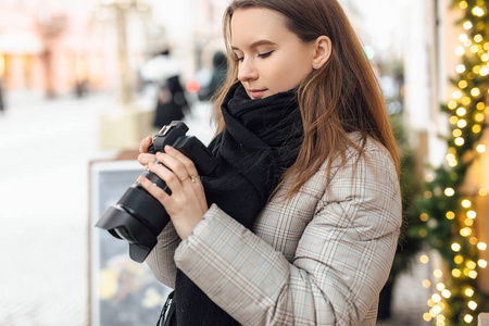 摄影师女孩走在街上，用快乐的脸照相机拍照。 戴上黑色围巾。 冬季秋装。