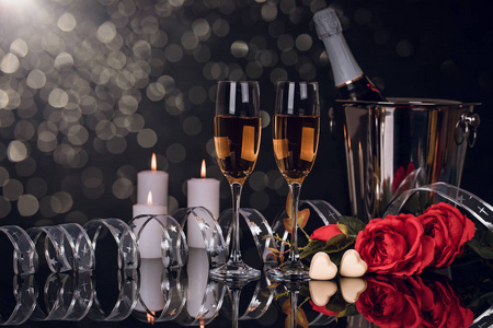 香槟瓶在桶里，有两个酒杯，一束玫瑰，心形巧克力和蜡烛，在黑色背景上发光。 爱情情人节概念