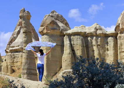 一个年轻的女人拿着一层蓝色的面纱，戴在她的头上，站在卡帕多西亚蜜谷巨大和古老的岩石之间。