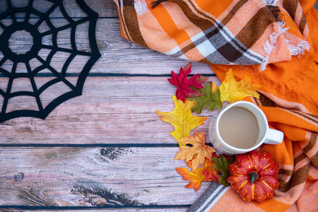 舒适的秋季概念背景与咖啡杯，留下橙色格子毯和蜘蛛网。 木质背景和复印空间的空间