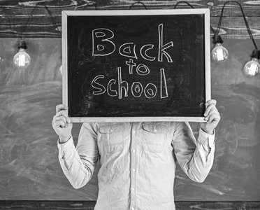 学年概念的开始。老师不露面把黑板和标题放回学校。男子欢迎学生, 黑板上的背景。老师在脸前拿着黑板。