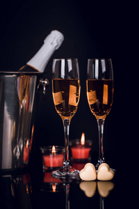 桶里的香槟瓶，两个酒杯，两个心形巧克力和黑色背景上的蜡烛。 爱情情人节概念