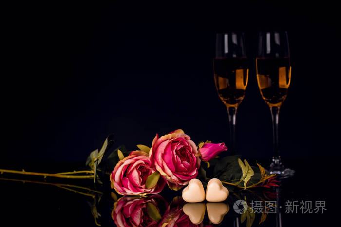 两杯香槟玫瑰和两颗心形巧克力在黑色背景上爱情人节的概念复制空间