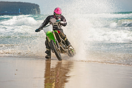 骑摩托车的人穿着防护服, 骑着摩托车在海上, 从车轮下飞溅而来