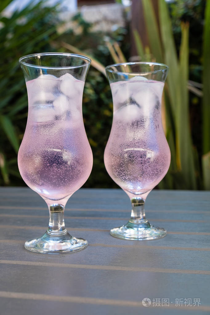 在花园里的木桌上放两杯粉红色的杜松子酒和补品