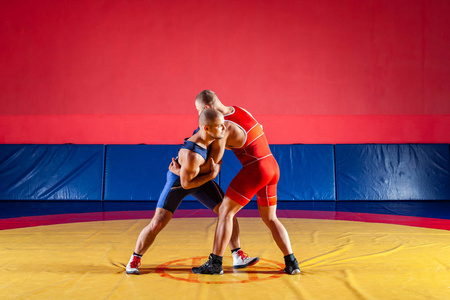 公平摔跤的概念。 两位身穿红蓝制服的罗马摔跤手在体育馆的黄色摔跤地毯上摔跤