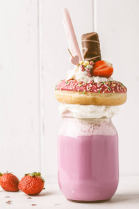粉红色草莓怪物奶昔鸡尾酒与甜甜圈和糖果在白色背景。 不健康的甜点概念。