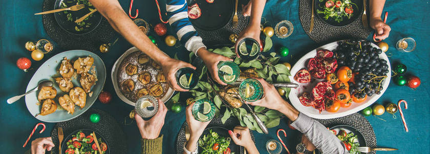 朋友聚会圣诞节或新年聚会晚餐在节日桌上。 平躺着的人手拿着杯子和饮料一起庆祝节日，视野开阔