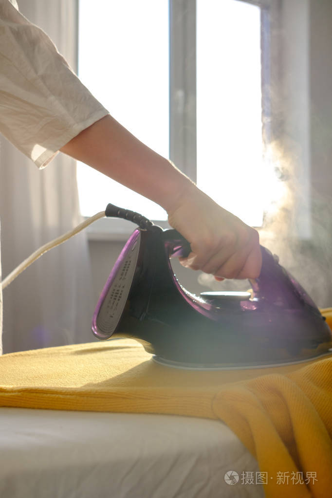 女孩在家熨衣服一件黄色夹克