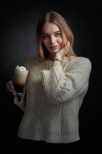 带着爱尔兰咖啡的迷人年轻女人。穿着毛衣的金发美女拿着一杯咖啡和奶油。