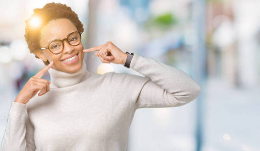年轻美丽的非裔美国妇女戴着眼镜，在孤立的背景上微笑，自信地展示和手指，牙齿和嘴。 健康概念。